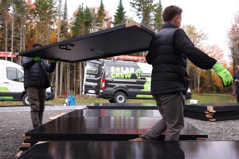 Greenfoot Solar Crew carrying a solar panel beside their service vehicles